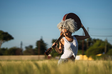 Chica guapa tatuada con pelo muy rizado posando en un campo de trigo con una guitarra acsutica