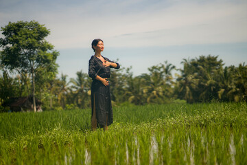 artistic portrait of young attractive and happy Asian woman outdoors at green rice field landscape dancing and doing spiritual meditation on beautiful nature background 