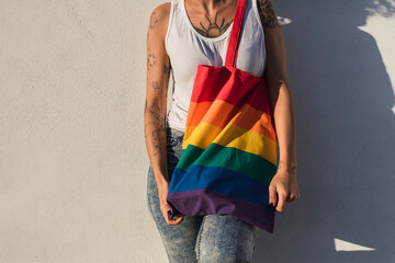 Chica delgada con pelo muy rizado delante de pared blanca posando feliz ocn una bolsa con la bandera de arco iris