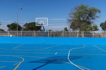 Cancha de baloncesto de color azul con tablero transparente rodeada de una verja blanca