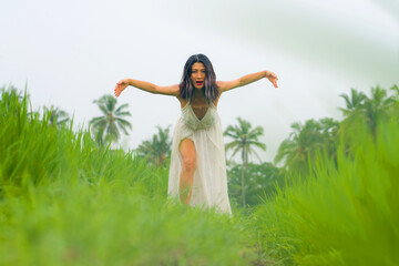artistic portrait of young attractive and happy Asian woman outdoors at green rice field landscape wearing elegant long dress dancing on beautiful nature carefree 