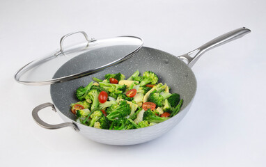 frying pan with fried vegetables and glass lid isolated on white