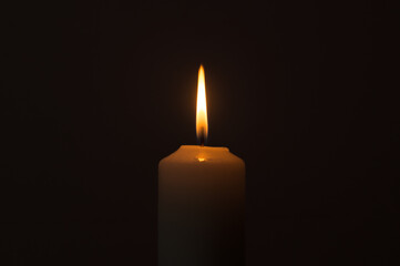 A burning candle flame isolated on black or dark background on table in church for Christmas,...