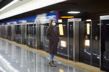 A woman in a medical face mask is waiting for an arriving train on the subway.