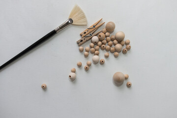 medium sized fan paint brush with black handle, two wooden clothes pins, and various sizes of plain wooden beads on a white canvas background