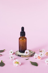 Concept of natural cosmetics for face, body and hair care on a pink background. Glass bottle with liquid on a pink background on a wooden stand, round cut of a tree trunk, near pink small flowers