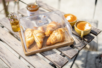 Croissants under the glass cloche with cups of coffee on the garden table. French style. Spend and enjoy time outdoors in the sun. 