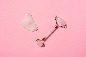 Jade face massage roller and gua sha on pink background.