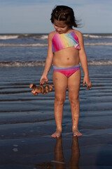 niña mira su muñeco sucio en la playa.