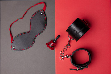 BDSM toys on a gray-red background with a bell. The sex ring is beautifully divided into different colors. Role-playing acts for adults. Sex shop
