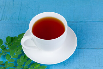 moringa tea in white ceramic cup and fresh green moringa leaf on blue wooden background. alternative healthcare and medical concept.
