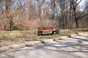 Panoramic view of the park alley with a wooden bench and a view of the bushes and trees.