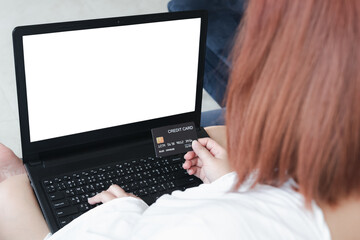 A woman holding a credit card, which is paying online, on a laptop, sitting on the sofa in the living room, at home with clipping path. The concept of online shopping.white screen notebook for mockup