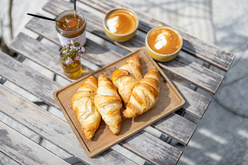 Croissants on the wood plate with cups of coffee and jam on the garden table. French rusticate style. Spend and enjoy time outdoors in the sun. 