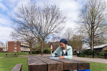 Black Muslim woman in park writing