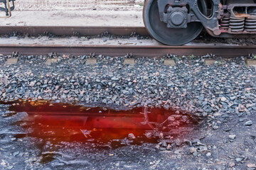 A puddle of red potash fertilizers after rain on crushed stones near the railway tracks on...