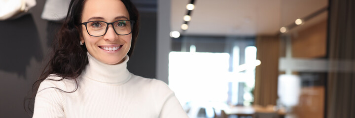 Brunette woman with glasses smiling and holding ballpoint pen over notebook