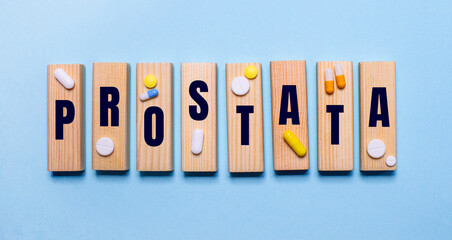 The word PROSTATA is written on wooden blocks on a light blue table near the pills. Medical concept