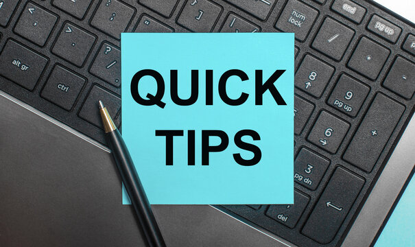The computer keyboard has a pen and a blue sticker with the text QUICK TIPS. Flat lay.