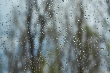 Rain drops falls on window glass with grey sky
