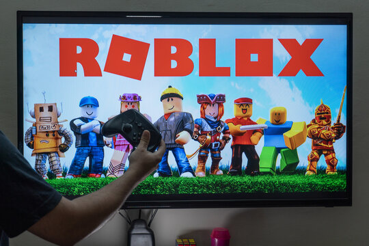 man with a controller standing in front of a PC console TV screen with a steam controller playing popular free to play game Roblox