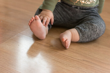 Obraz na płótnie Canvas Toddler baby sitting on laminate wood floor with bare feet; about to crawl away meeting a developmental milestone