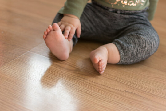 Toddler baby sitting on laminate wood floor with bare feet; about to crawl away meeting a developmental milestone © Julia Beatty