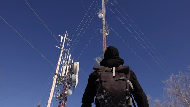 Locked down video of an avid explorer marveling at the 4G and 5G telecommunication towers on mountains, with antennas attached to them.