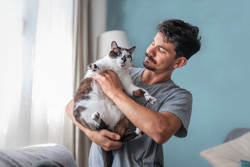 young man hugs a black and white cat  with blue eyes