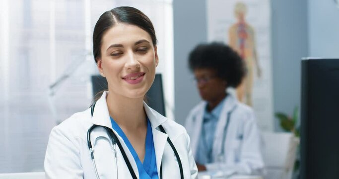 Close up portrait of joyful positive young woman doctor looking at camera and smiling while working in clinic. Happy female healthcare worker in white medical coat with smile on face, medic concept