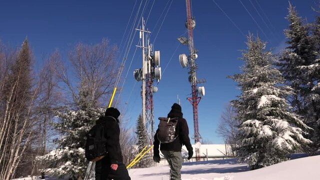 Locked down shot of two young explorers working on a documentary, as they arrive at telecommunication tower base, and take off their travel bags. 