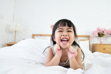 Adorable happy Asian toddler girl lie in bed with smiling face, happiness moment after wake up