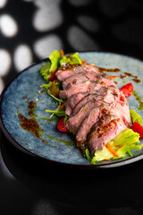 Grilled duck meat with salad on a grey plate on a black background.