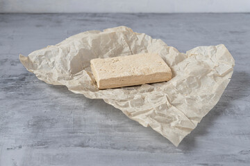 Peanut halva lying on parchment paper on a gray background. Copy space. Traditional national dessert. Turkish, Arabic, Oriental cuisine.
