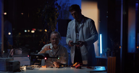 Adult repairman fixing drone in office talking to colleague cooperating. Handsome young man in lab coat flying drone technology testing in research office. Teamwork.