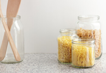 Variety of italian pasta in glass jars uncooked on white kitchen background, closeup, zero waste, eco friendly, balanced diet food, healthy clean eating concept