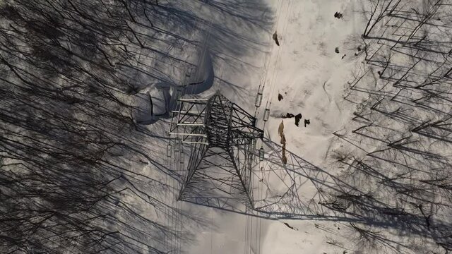 Take an interesting look at this zooming out aerial shot, featuring a tall telecommunication signals tower, located in snowy area with barren trees.