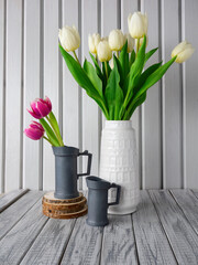Rural still life,fresh bunch white pink tulips in white vase and 2 steel jugs,green leaves foliage,on striped wooden boards background,hand painted in light dark gray.Rustic interior poster,copy space