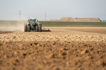 Obraz premium agricultural machinery works in the field. A tractor with a plow and a cultivator cultivates the land before sowing wheat and other cereals. The farmer plows the land very nicely and carefully.