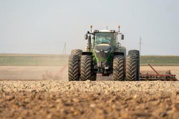 agricultural machinery works in the field. A tractor with a plow and a cultivator cultivates the land before sowing wheat and other cereals. The farmer plows the land very nicely and carefully.