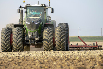 A large tractor close-up with a plow working in a field on a summer day against a clear blue sky. Tillage. A professional tractor driver does his job. The beginning of sowing works.