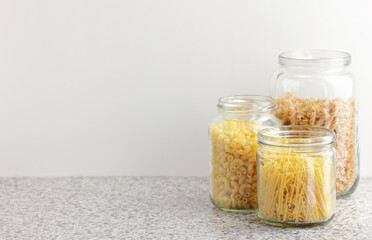 Variety of italian pasta in glass jars uncooked on white kitchen background, closeup, zero waste, eco friendly, balanced diet food, healthy clean eating concept