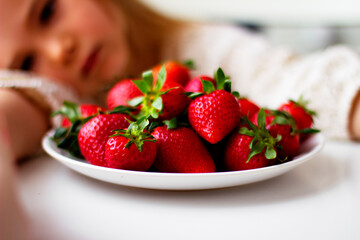 Cute little girl eating fresh strawberry in the kitchen. Healthy vitamin snack for kids. Ripe fresh berries. Harvest season. Natural vitamins .