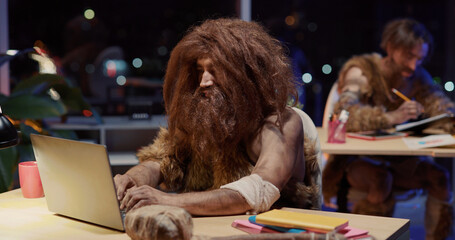 Portrait of confident savage man in cave animal clothes using laptop interacting learning technology looking smart to camera. Corporate people. Homo sapiens evolution.
