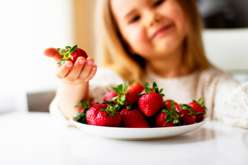 Cute little girl eating fresh strawberry in the kitchen. Healthy vitamin snack for kids. Ripe fresh berries. Harvest season. Natural vitamins .