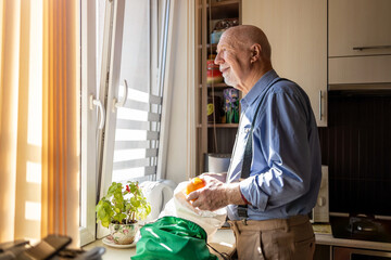 Senior man in kitchen at home looking out of window
