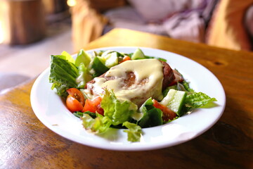 Fried fish fillet with cheese sauce topping and sliced vegetables on dish