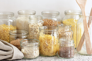 Variety of cereals, grains, pasta, seeds in glass jars uncooked on white kitchen background, closeup, zero waste, eco friendly, balanced diet food, healthy clean eating concept