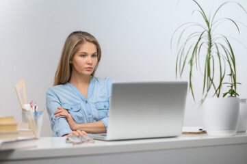 A girl with a laptop is studying at an online school. White room background