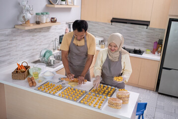 asian muslim couple making nastar snack cake together in the kitchen during ramadan for eid...